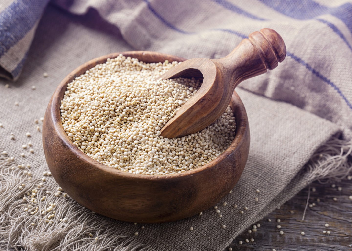 uncooked quinoa with scoop in wooden bowl