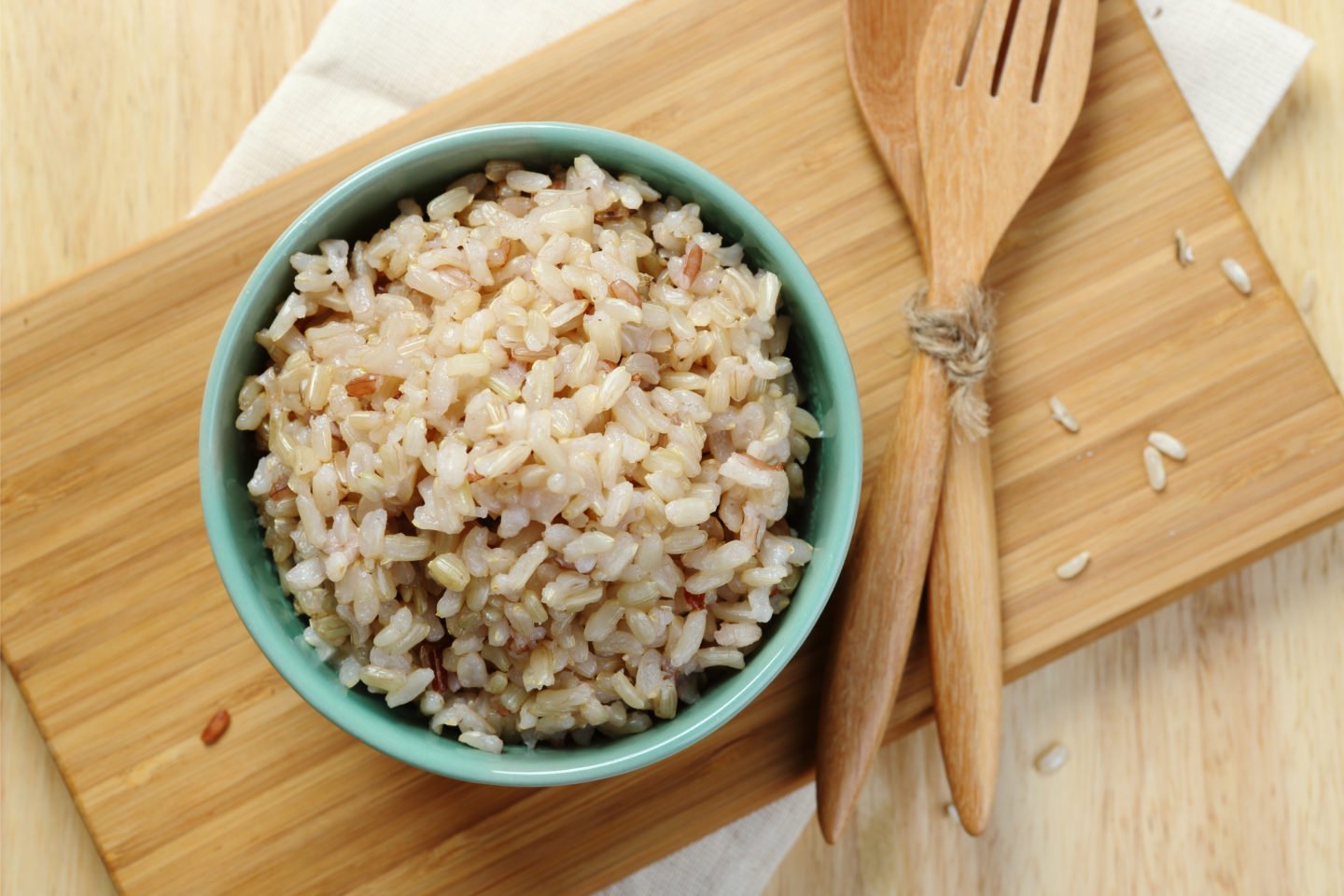 bowl of brown rice on wooden tray with utensils