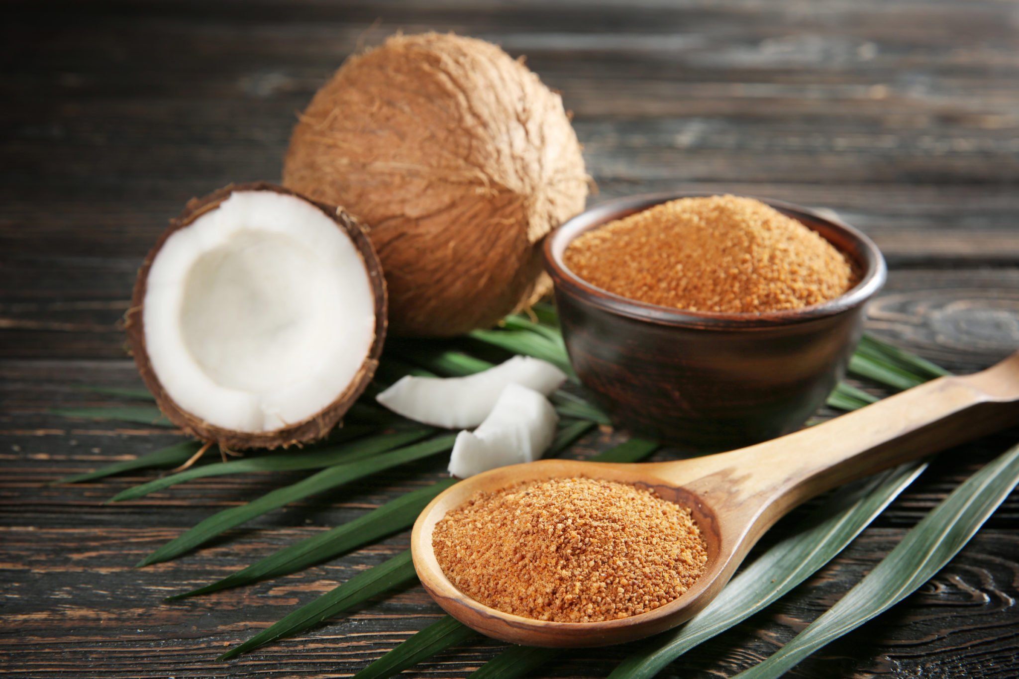 coconut sugar in a black bowl and huge spoon pictured with fresh coconuts