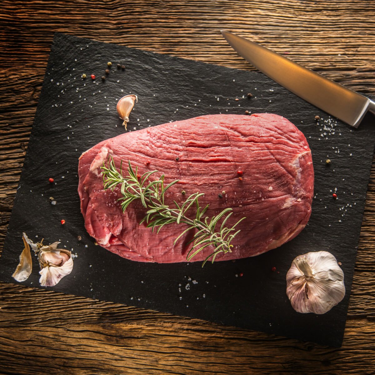 uncooked flank steak with herbs on cutting board