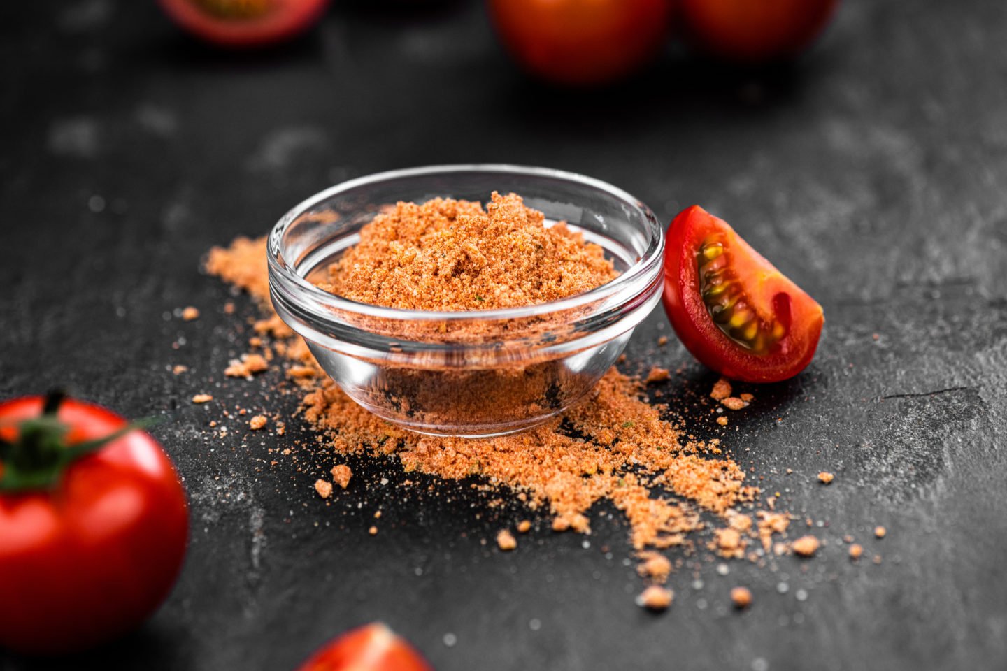 tomato powder in glass bowl with fresh tomatoes