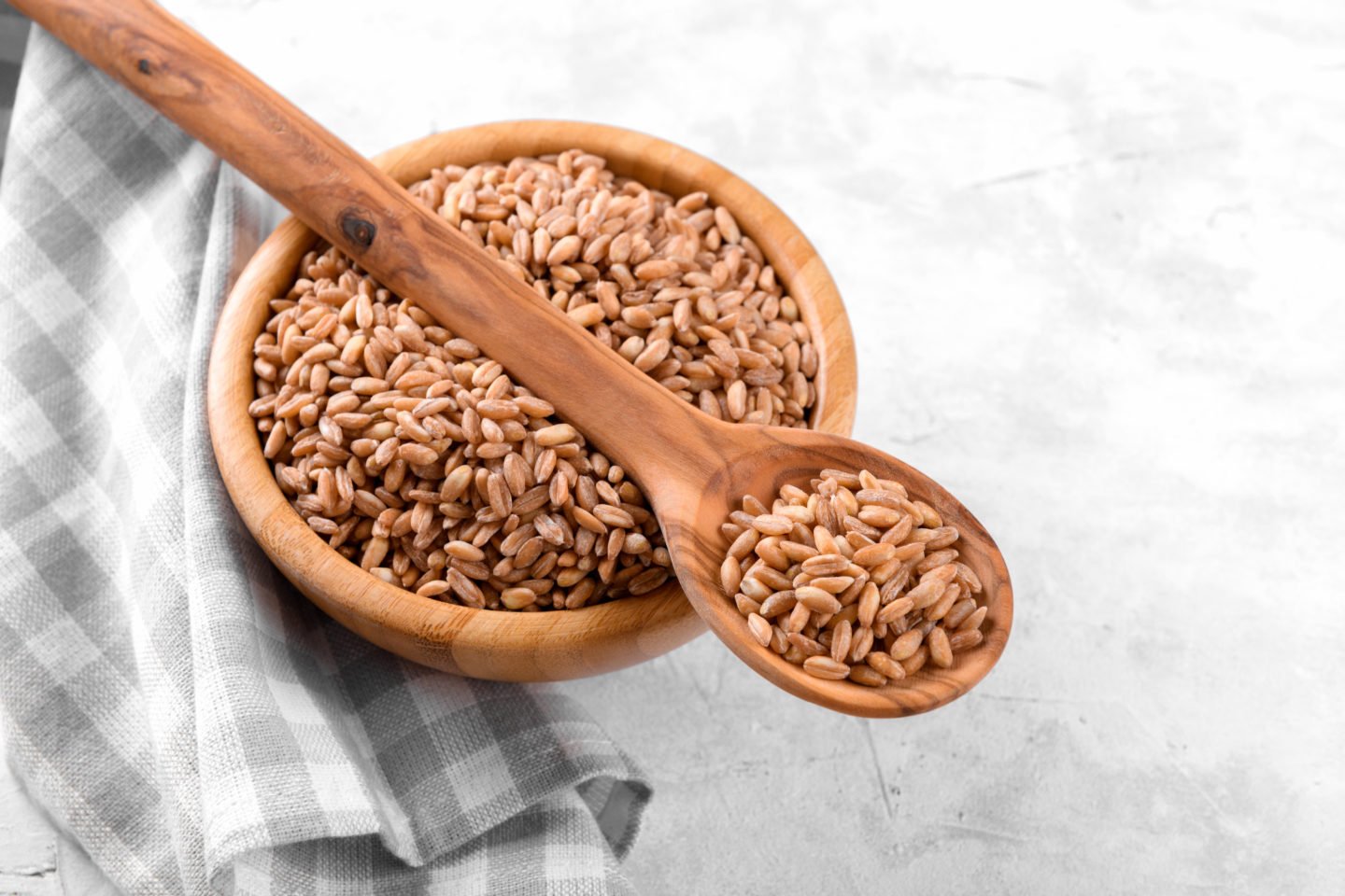 bowl of uncooked farro with wooden spoon