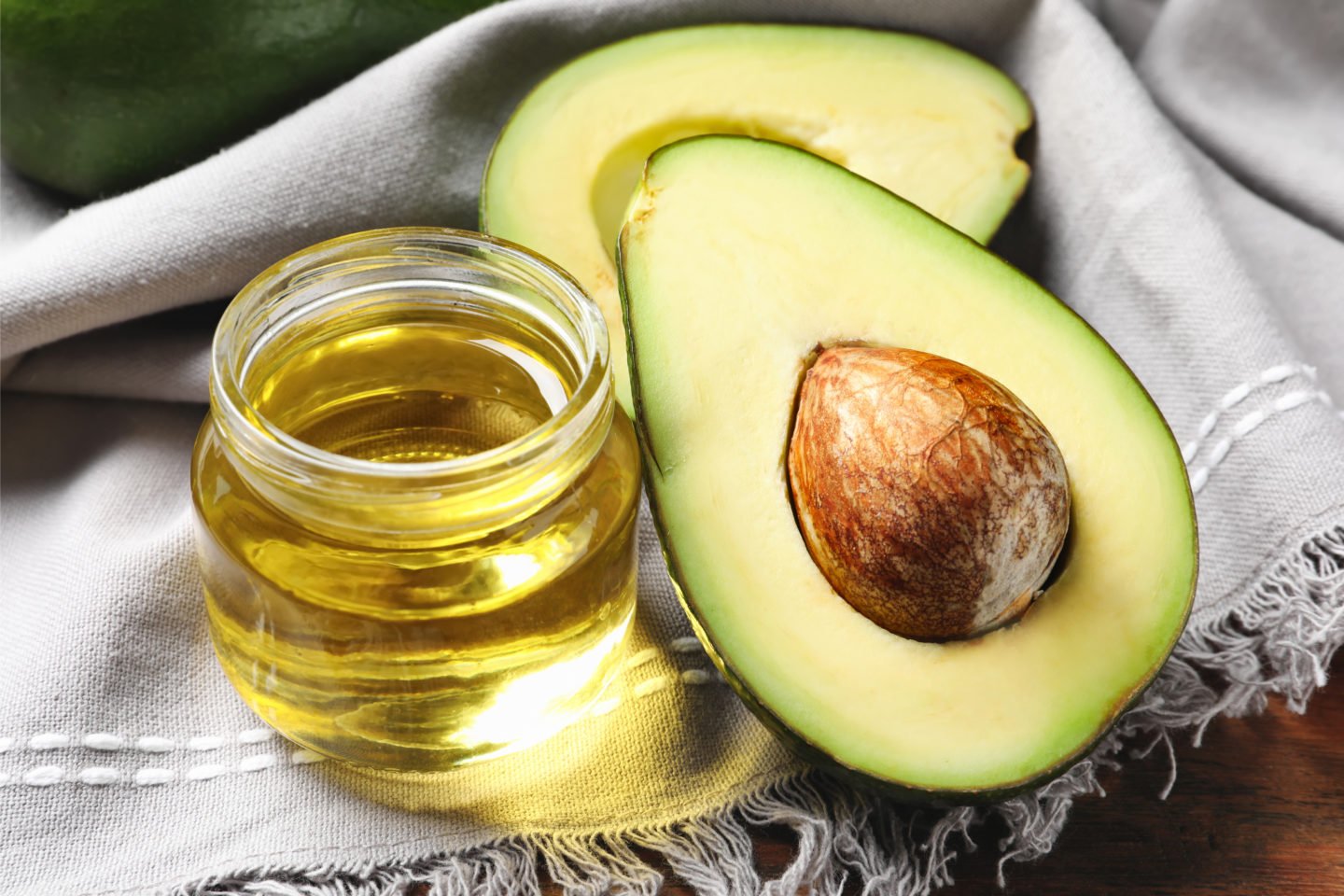 avocado oil in glass jar beside ripe avocado