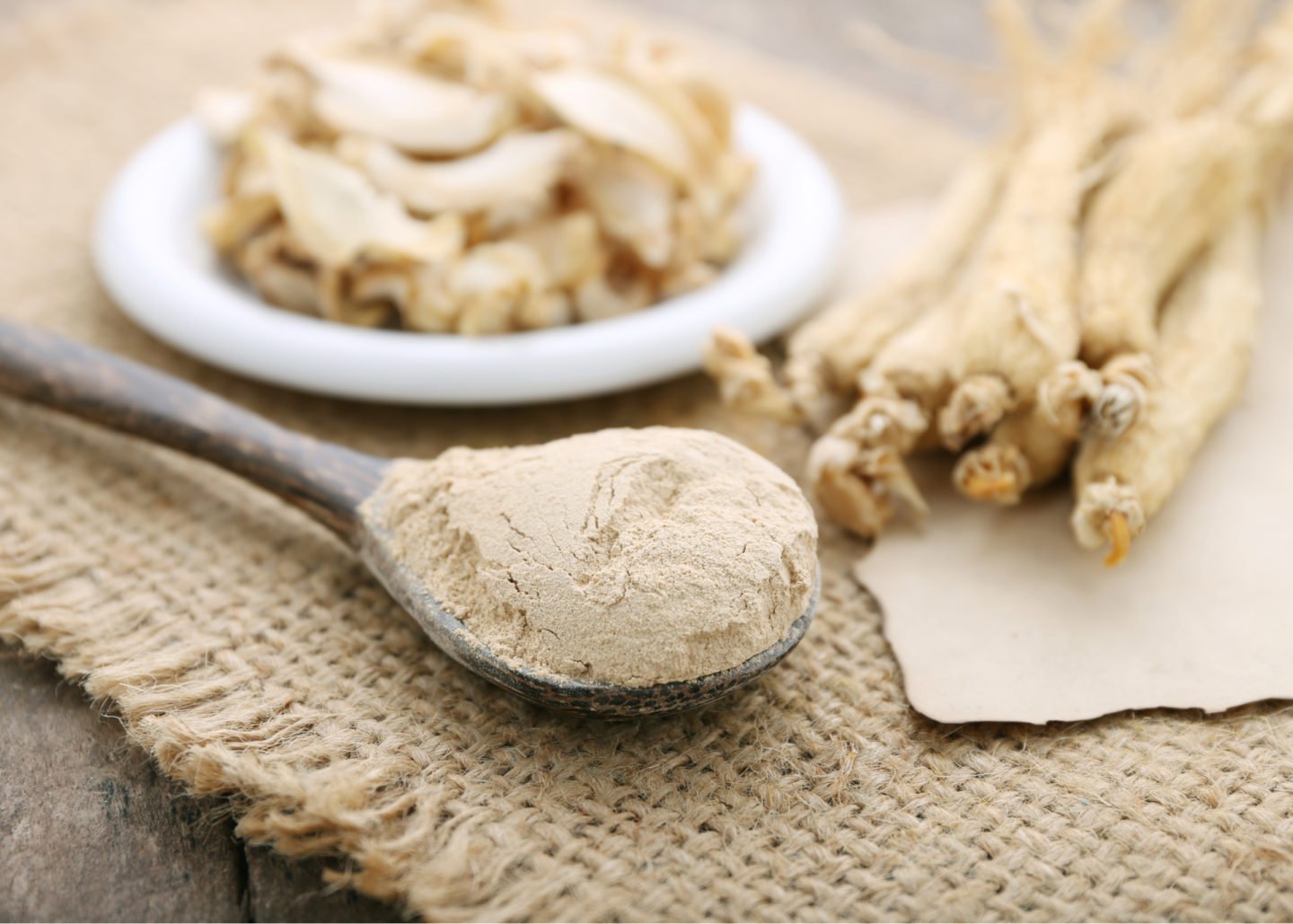 ginseng powder in a spoon alongside ginseng roots