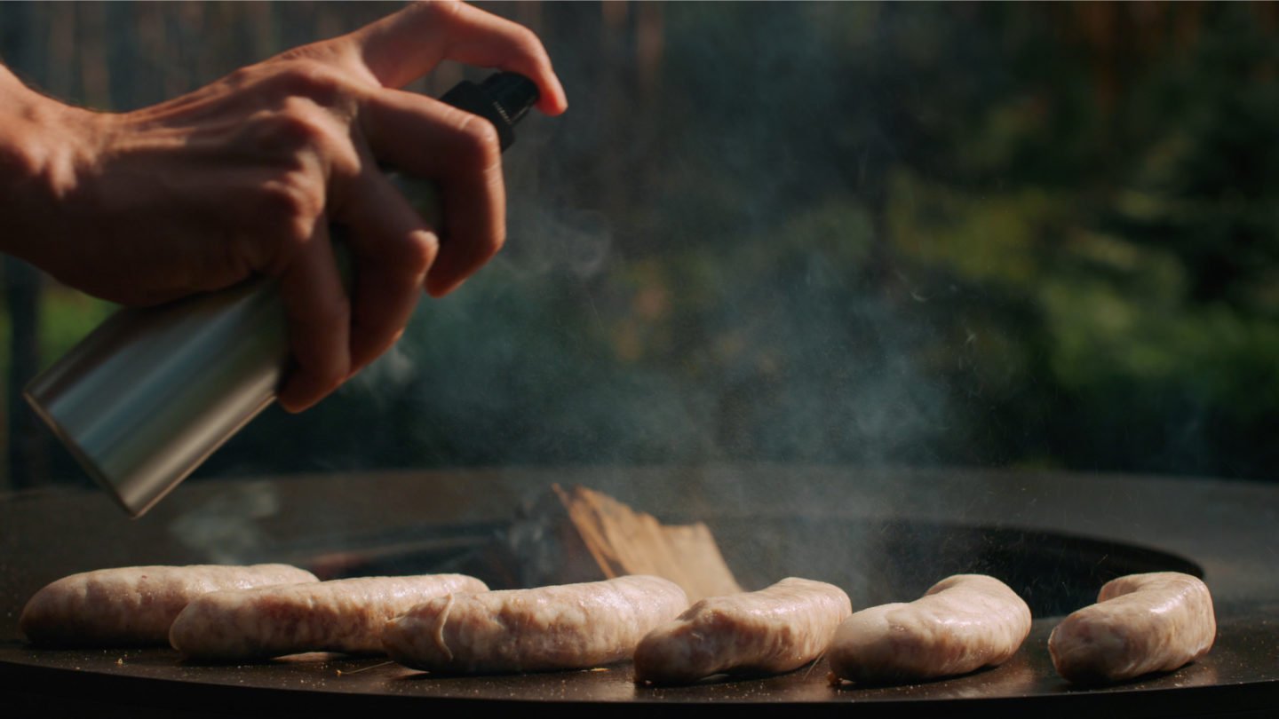 Man Using Cooking Spray On Sausages