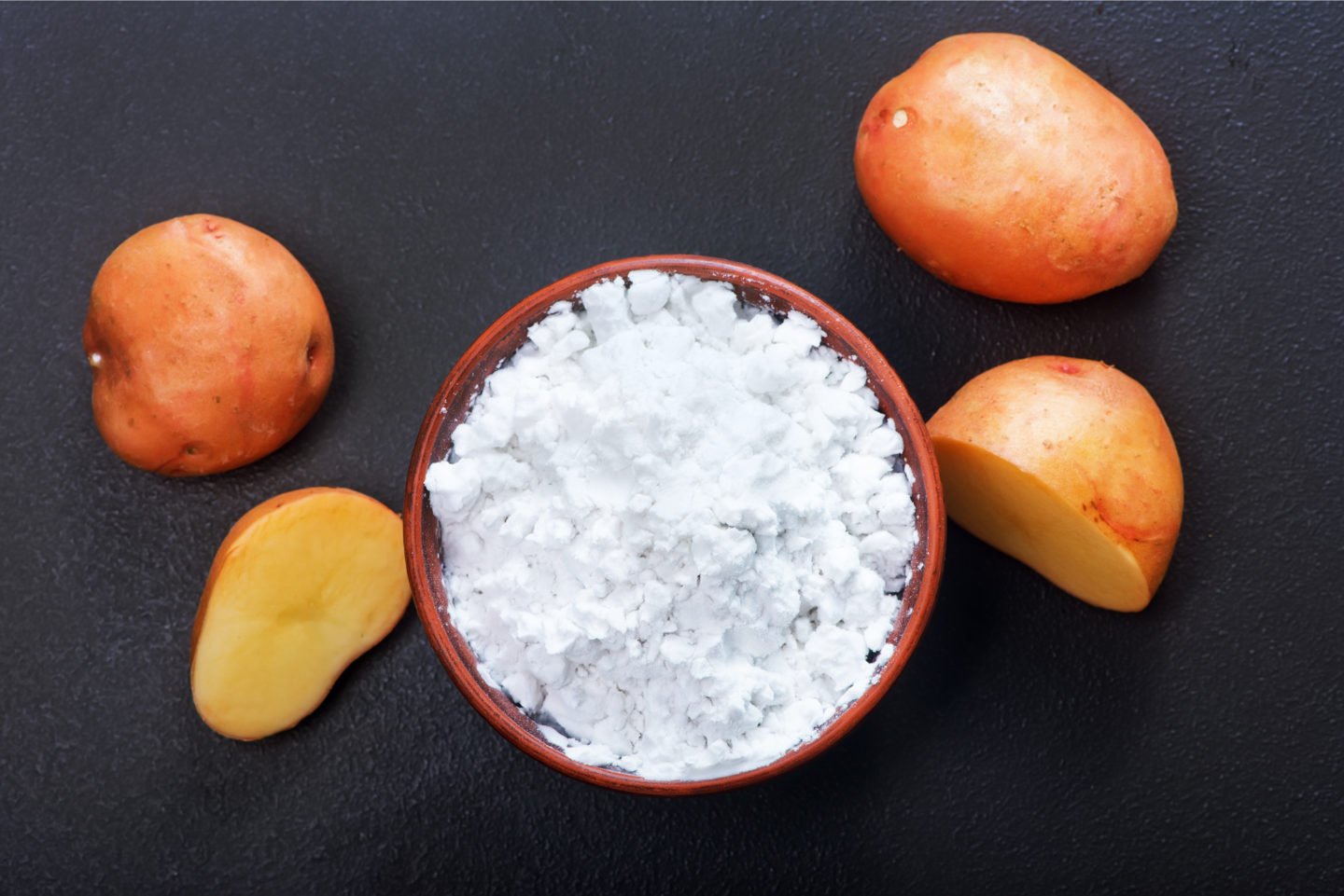 potato starch in wooden bowls surrounded by raw potatoes