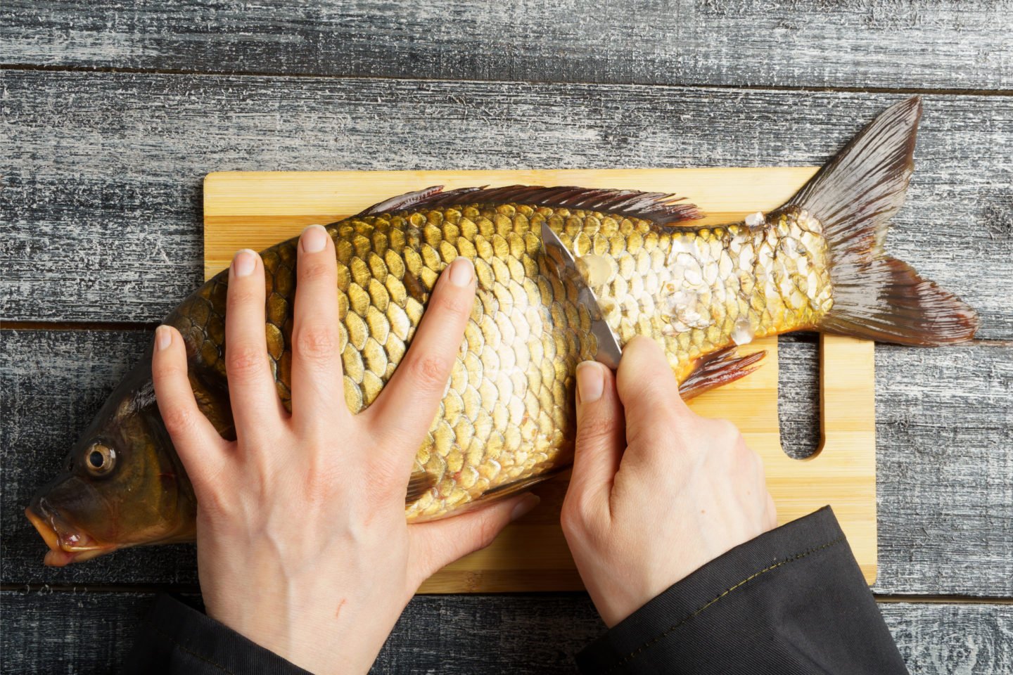 Scaling Fresh Carp On Cutting Board