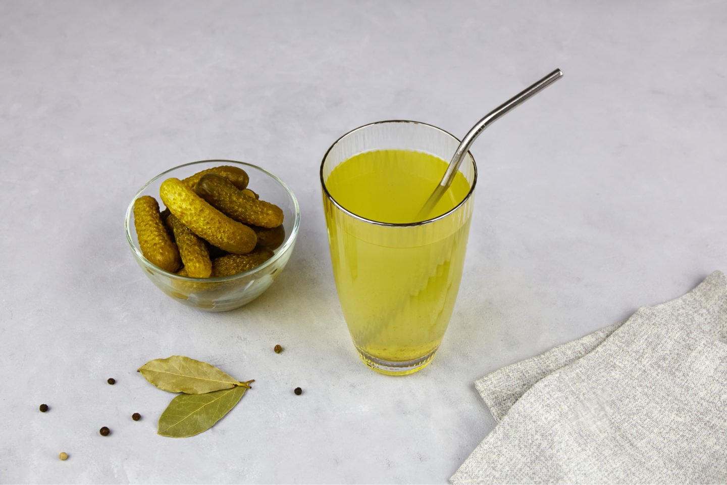 pickle juice in a glass with a bowl of pickled cucumbers
