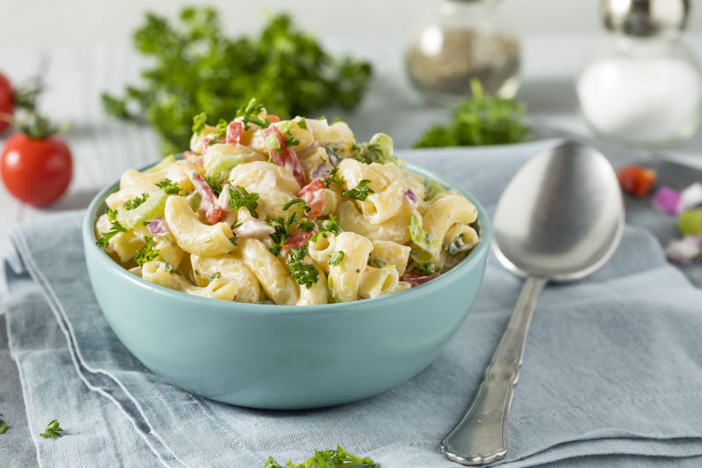 bowl of cold macaroni salad with tomato, onion, celery and parsley