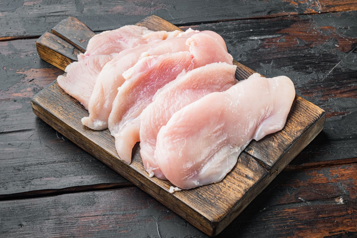 raw chicken cutlets on dark wooden board