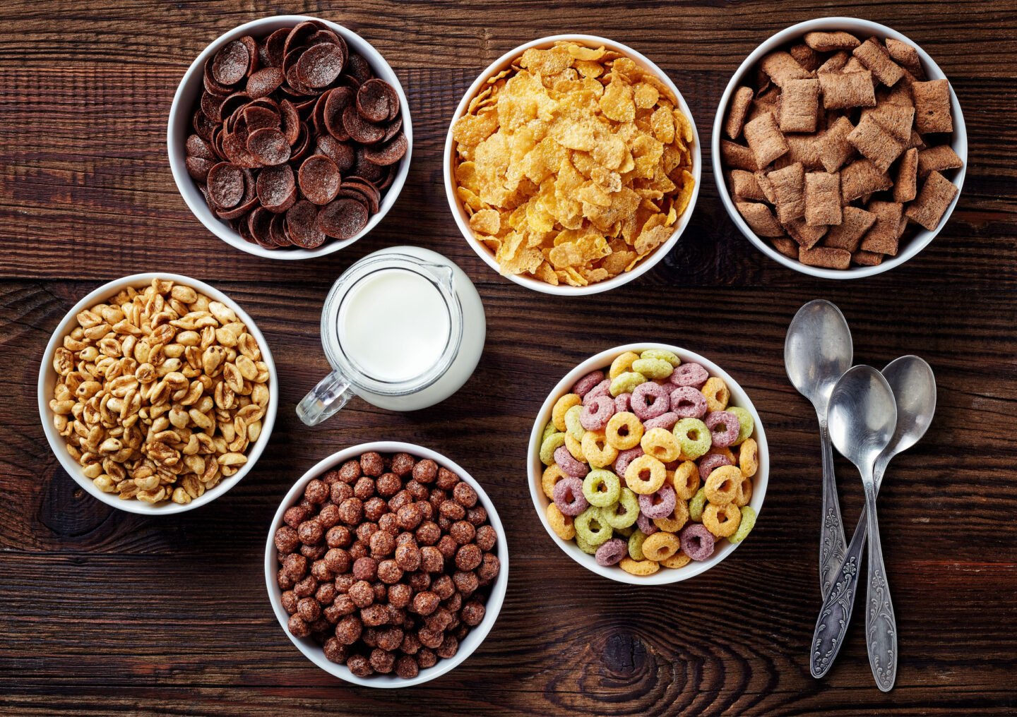 bowls of different breakfast cereals with jug of milk