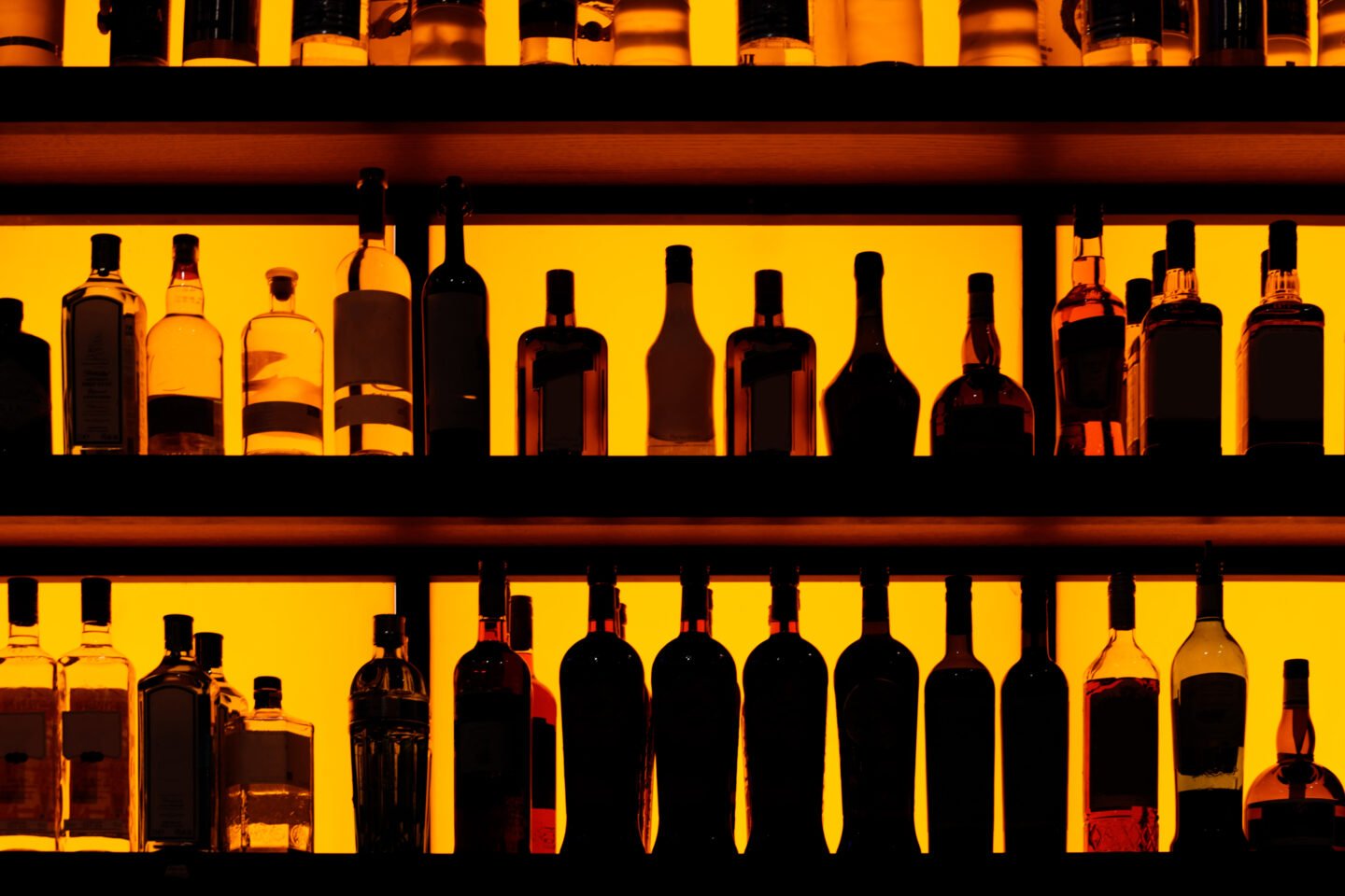 Rows,Of,Bottles,Sitting,On,Shelf,In,A,Bar,,Yellow