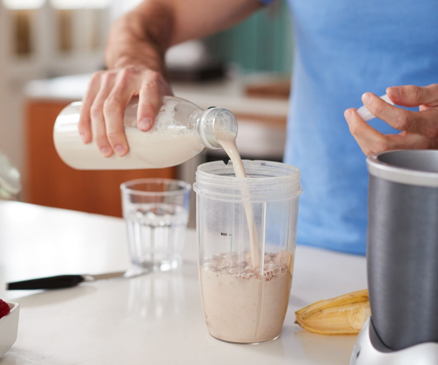 man pouring oatmilk into smoothie