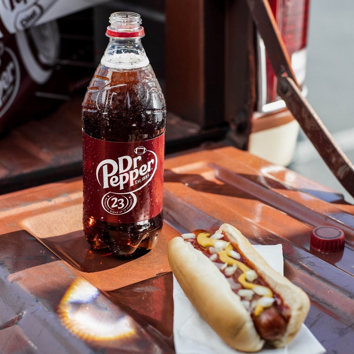 opened bottle of dr pepper on table beside hotdog bun