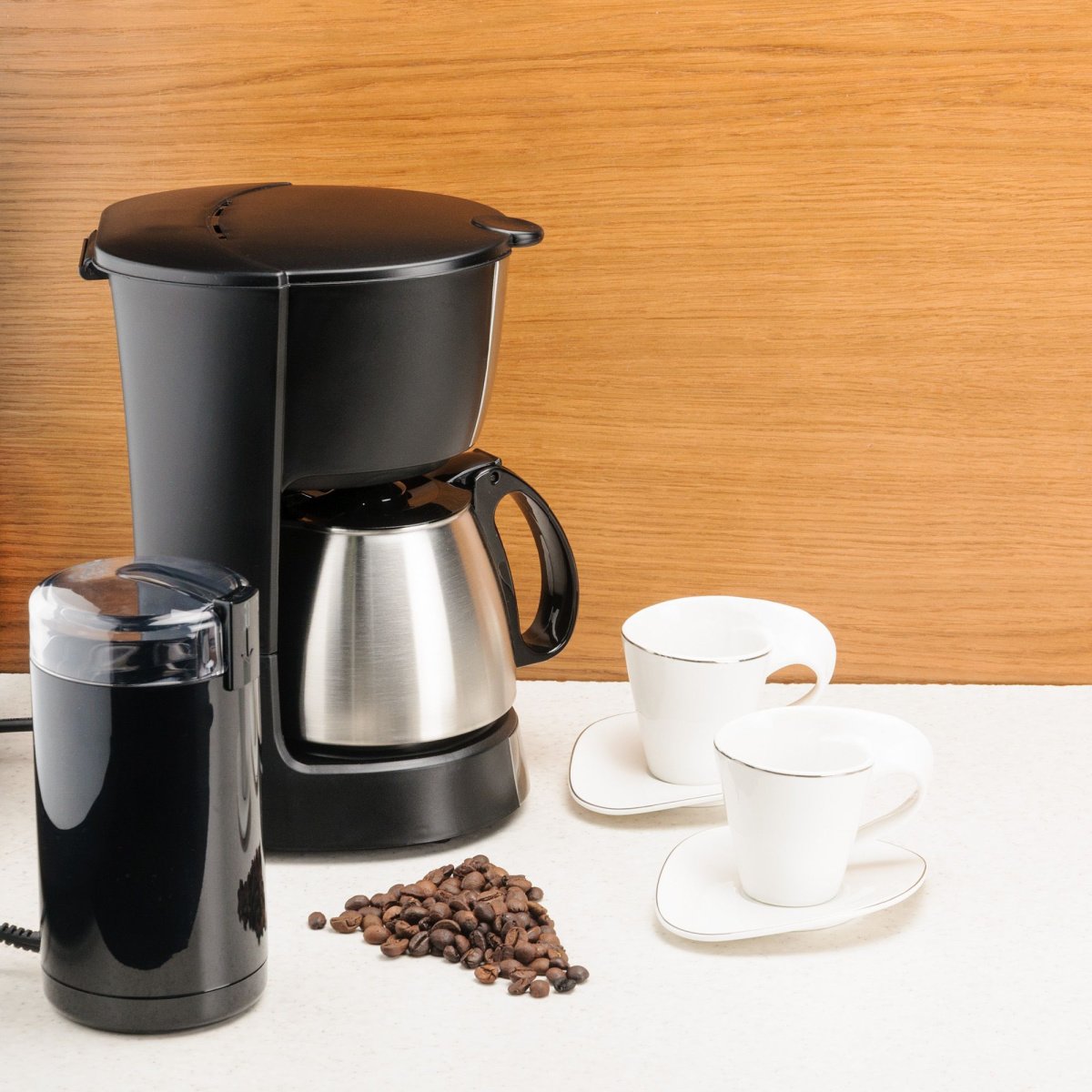 stainless steel carafe coffee maker on table with cofee beans and cups