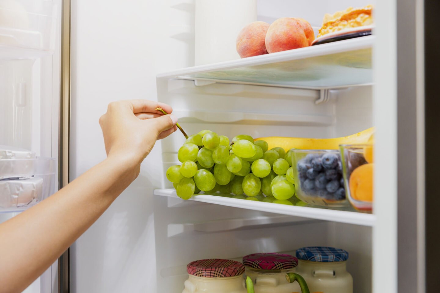 woman takes green grapes from fridge
