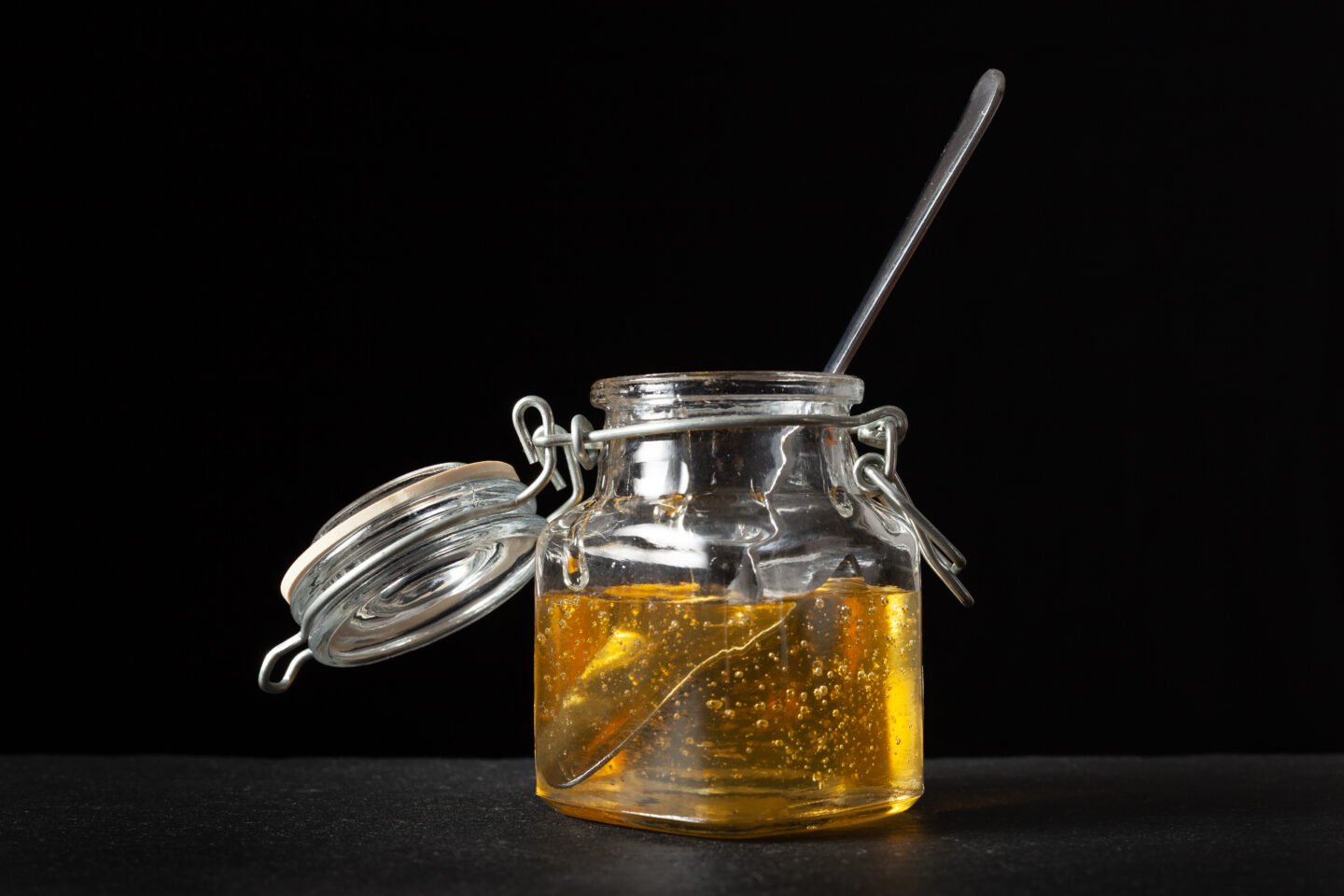 Agave,Syrup,In,Glass,Jar,With,Spoon,Inside.,Black,Background