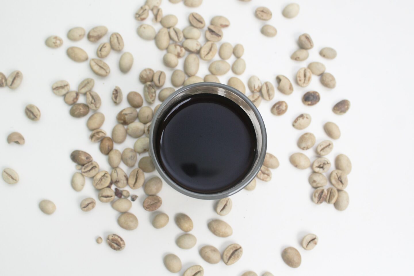 brewed white coffee in glass surrounded by white coffee beans