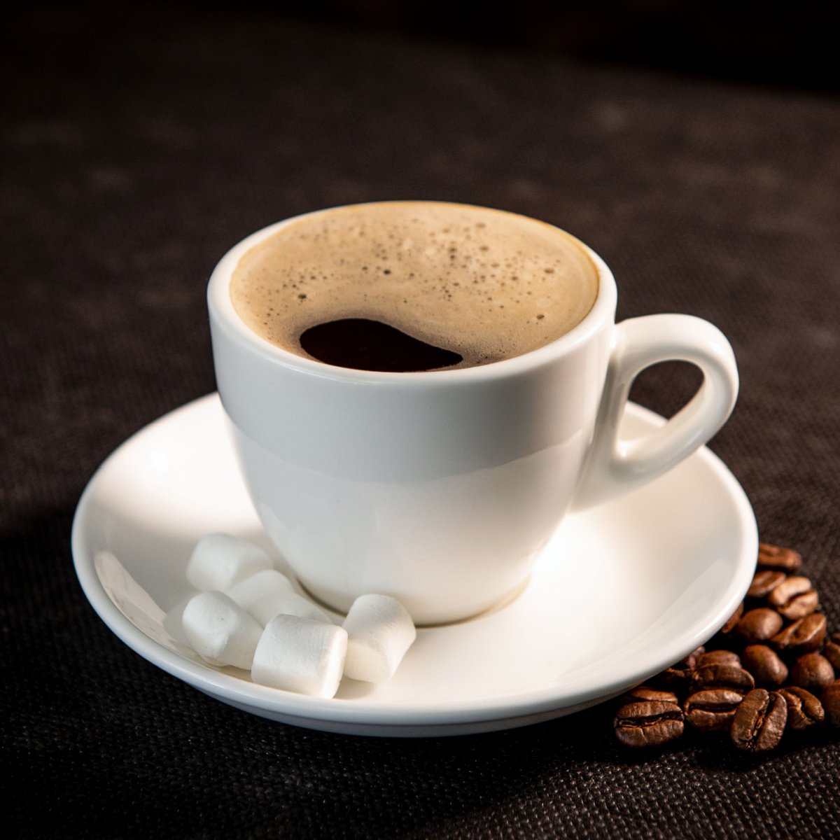 cup of coffee on white saucer with marshmallows and coffee beans