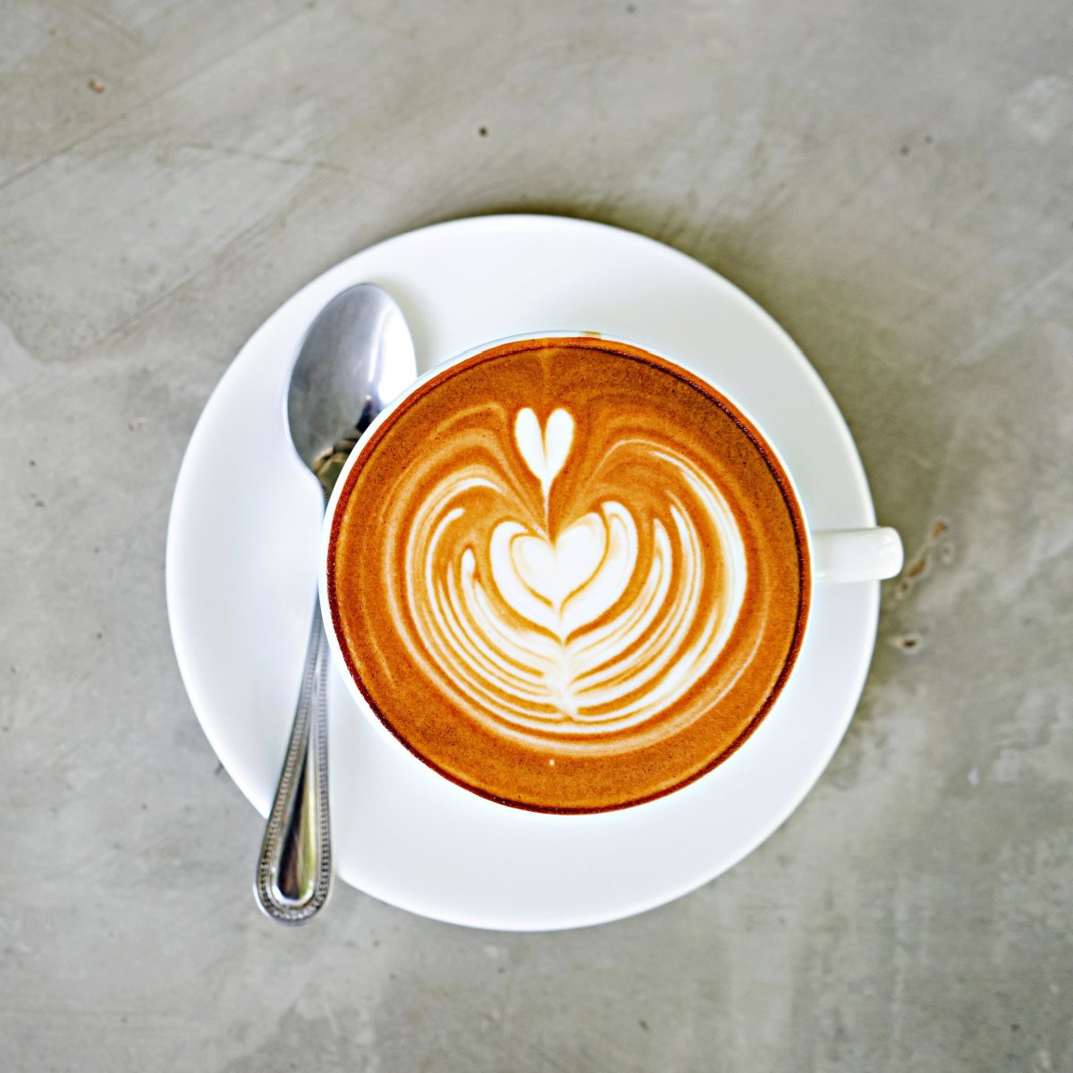 cup of freshly made latte with art on marble surface with spoon on saucer