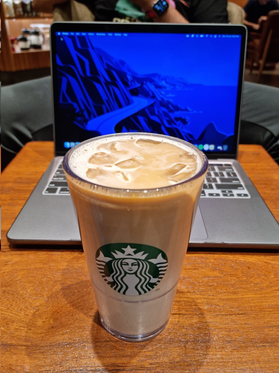 cup of starbucks iced flat white on wooden table in front of laptop