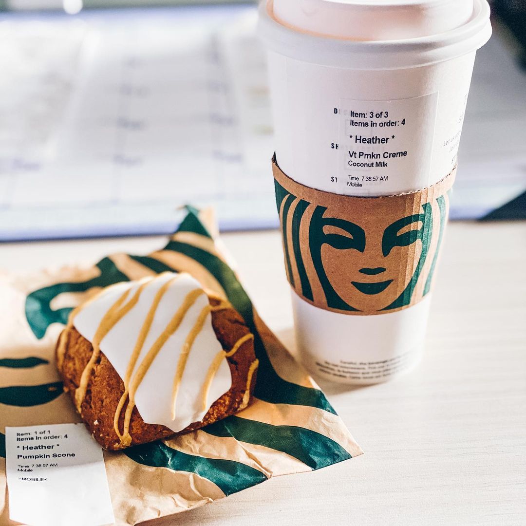 cup of starbucks pumpkin spice steamer on table beside pumpkin scone