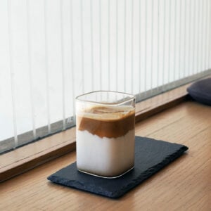 dirty coffee in square glass on wooden saucer and table