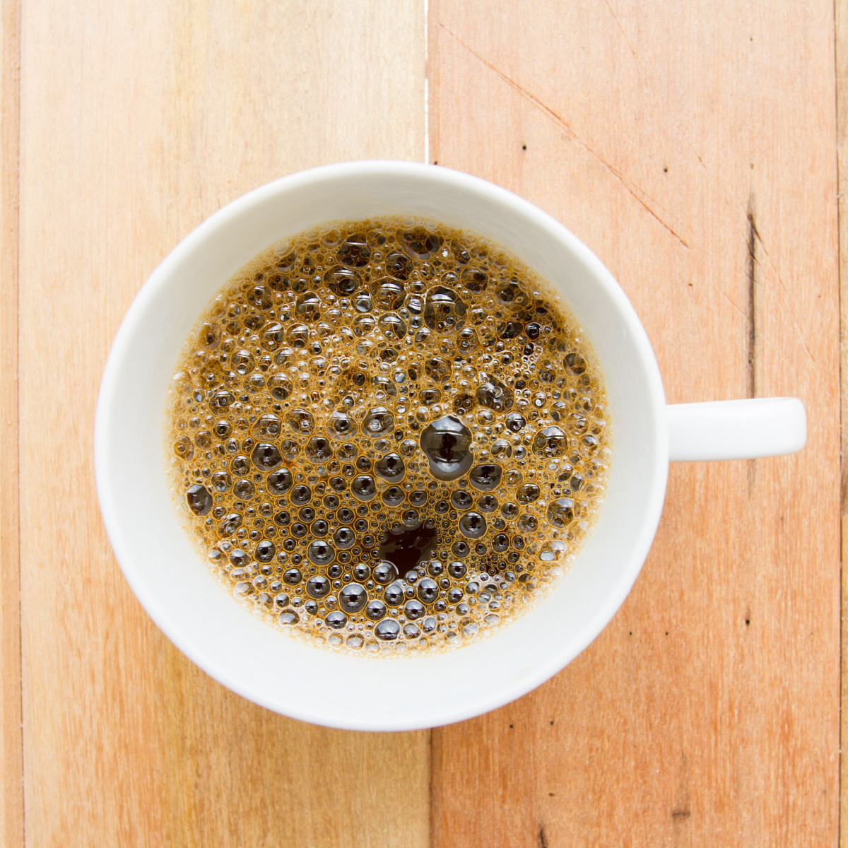 freshly brewed black coffee in white mug with bubbles on top