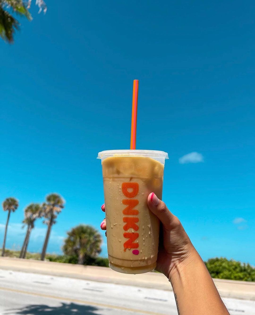 hand holding cup of dunkin donuts caramel swirl iced coffee beach background