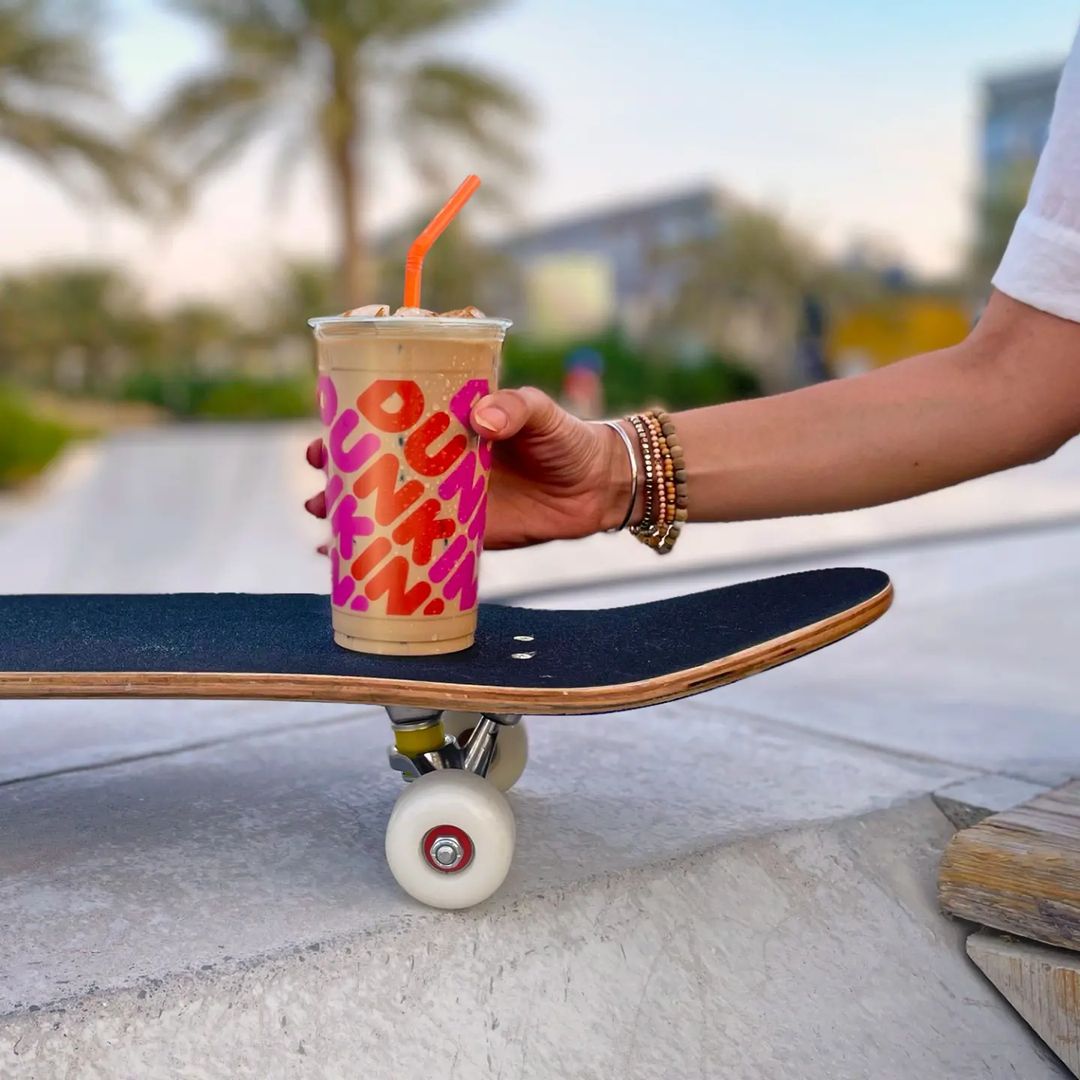 hand holding cup of dunkin donuts iced coffee on top of skateboard 1