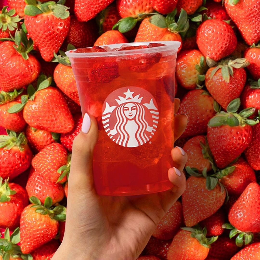 hand holding cup of starbucks strawberry acai refresher with strawberries in background