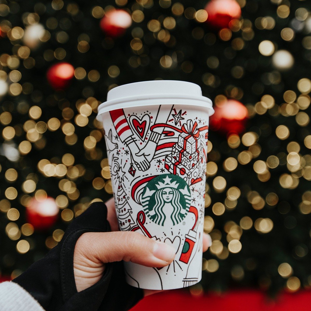 hand holding starbucks hot cup christmas tree in background