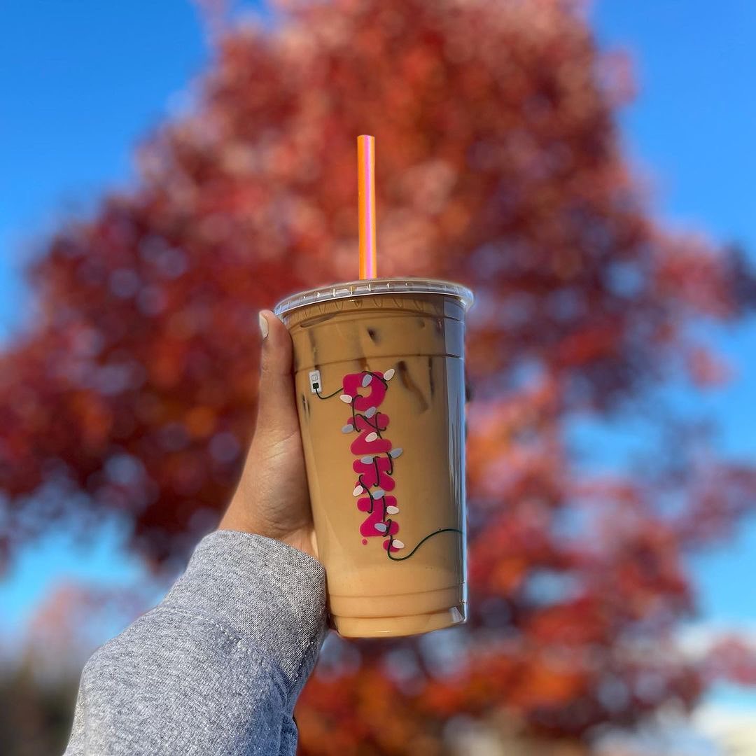 hand holding up cup of dunkin donuts iced cappuccino red tree in background