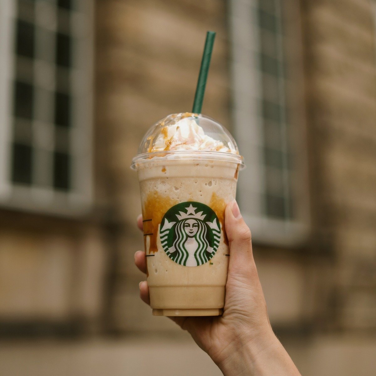 hand holding up cup of starbucks frappuccino stone building in background