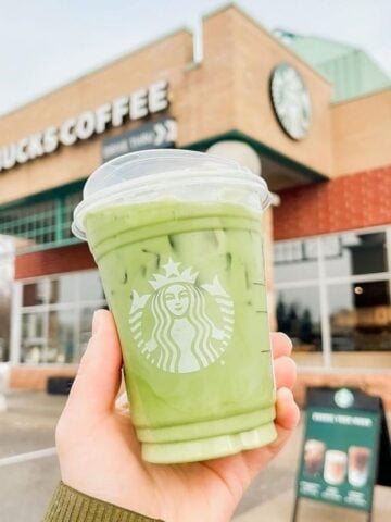 Hand Holding Up Cup Of Starbucks Iced Matcha Latte In Front Of Starbucks Branch 360x480