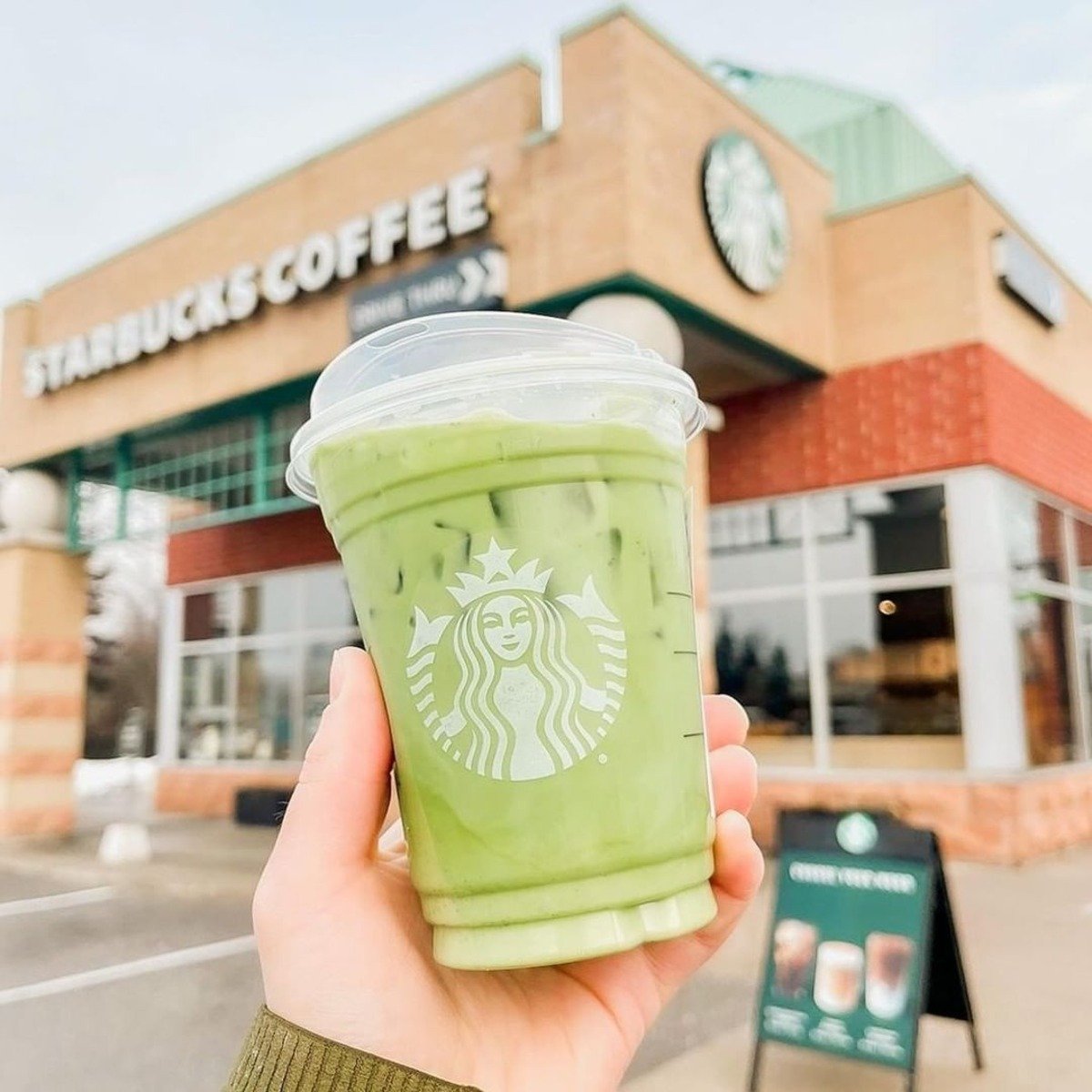 hand holding up cup of starbucks iced matcha latte in front of starbucks branch