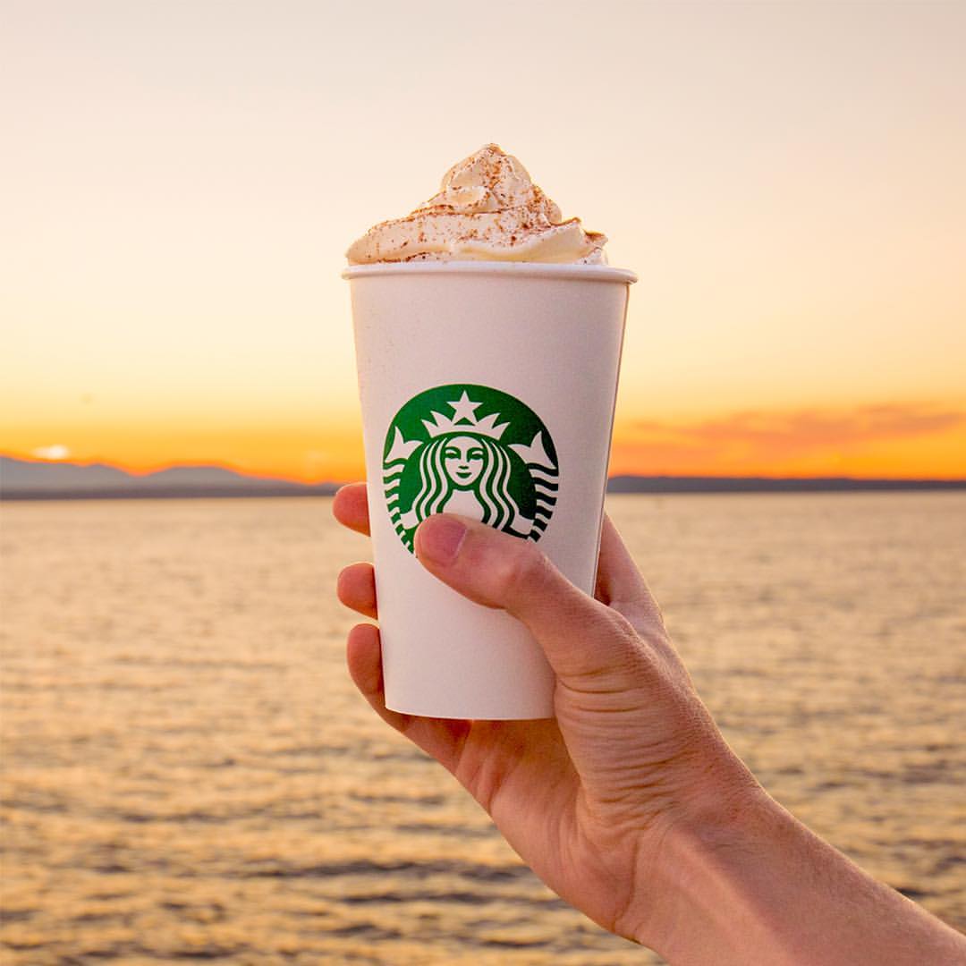 hand holding up cup of starbucks pumpkin spice latte to sunset