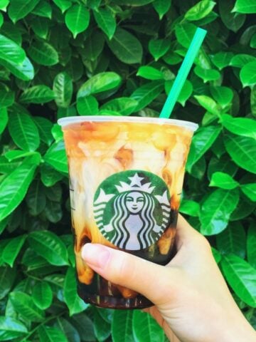 Hand Holding Up Cup Of Starbucks Vanilla Sweet Cream Cold Brew Green Leafy Background 360x480
