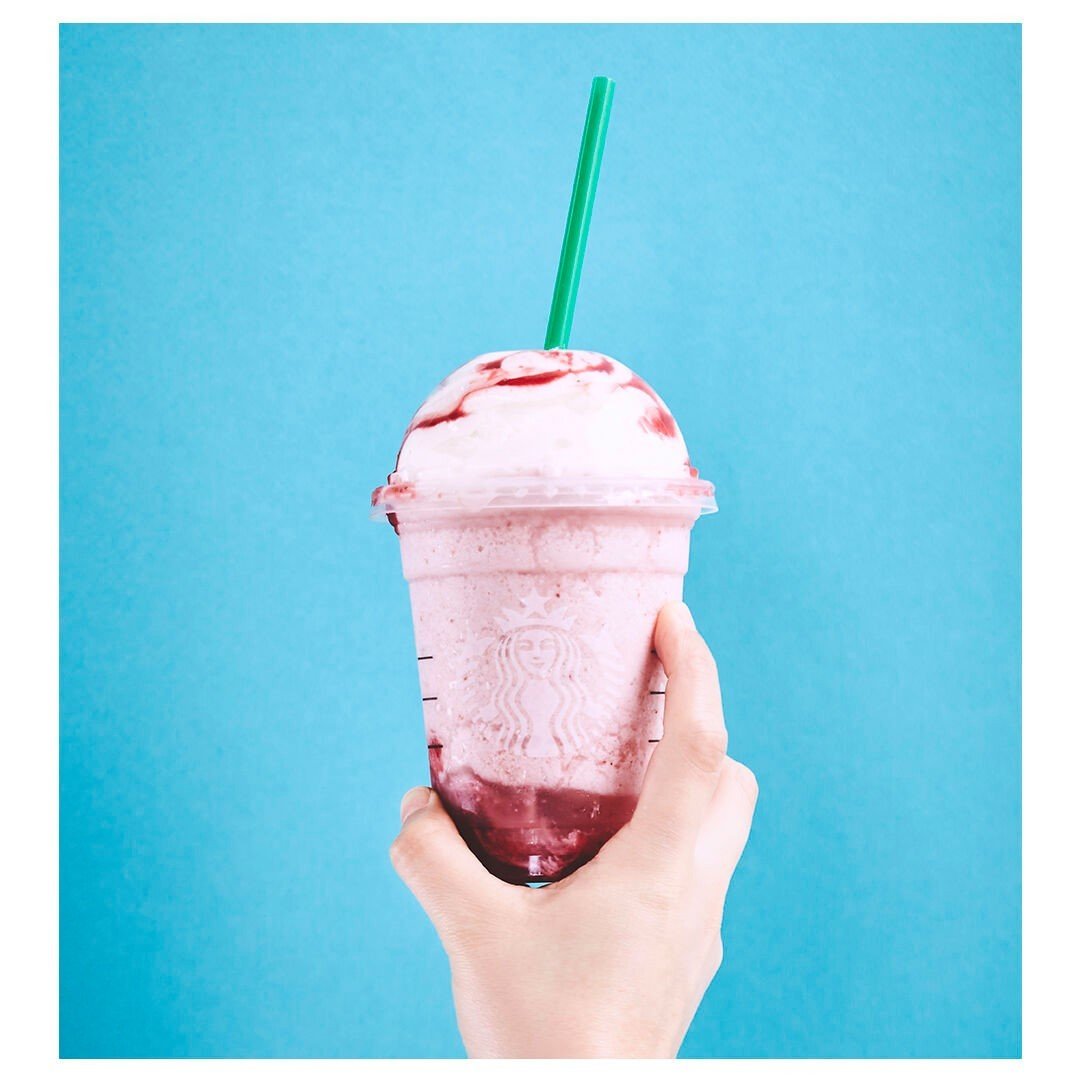 hand holding up cup of strawberry creme frappuccino blue background