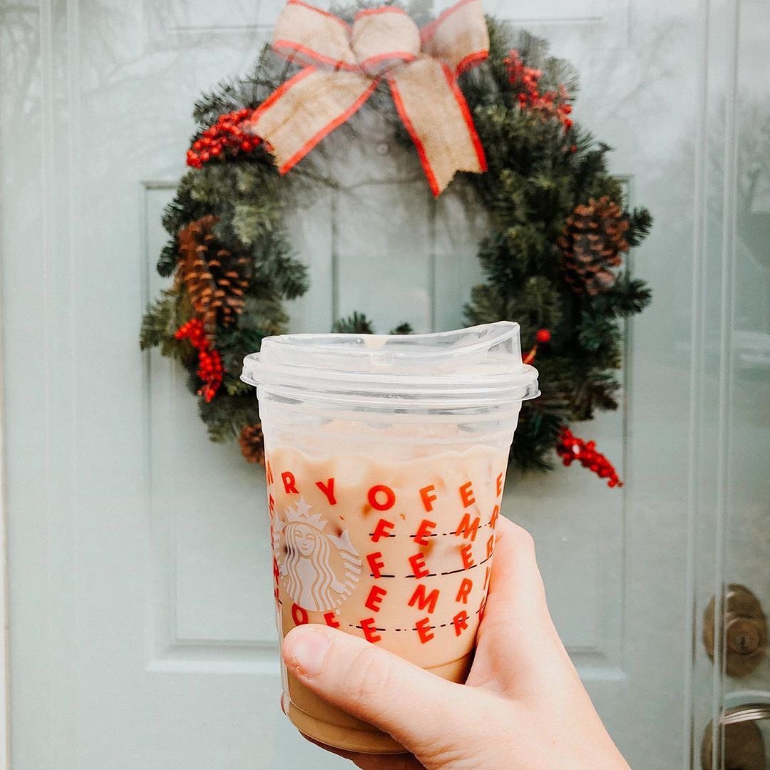 hand holding up starbucks cup of iced coffee in front of door and mistletoe