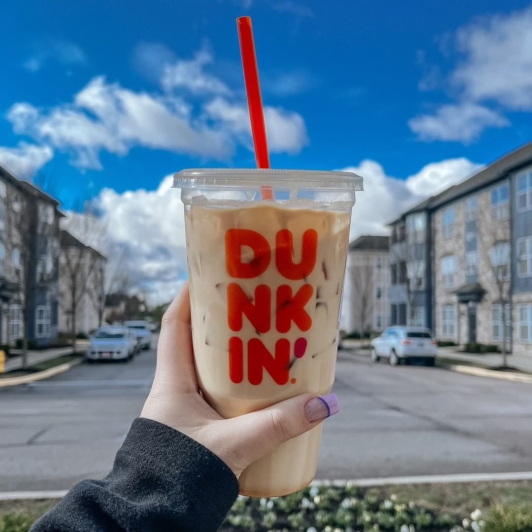 hand in sweater holding up cup of dunkin donuts iced coffee