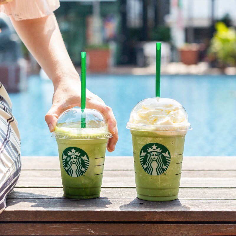 hand reaching for cup of starbucks green tea cream or matcha blended cream on wooden surface poolside