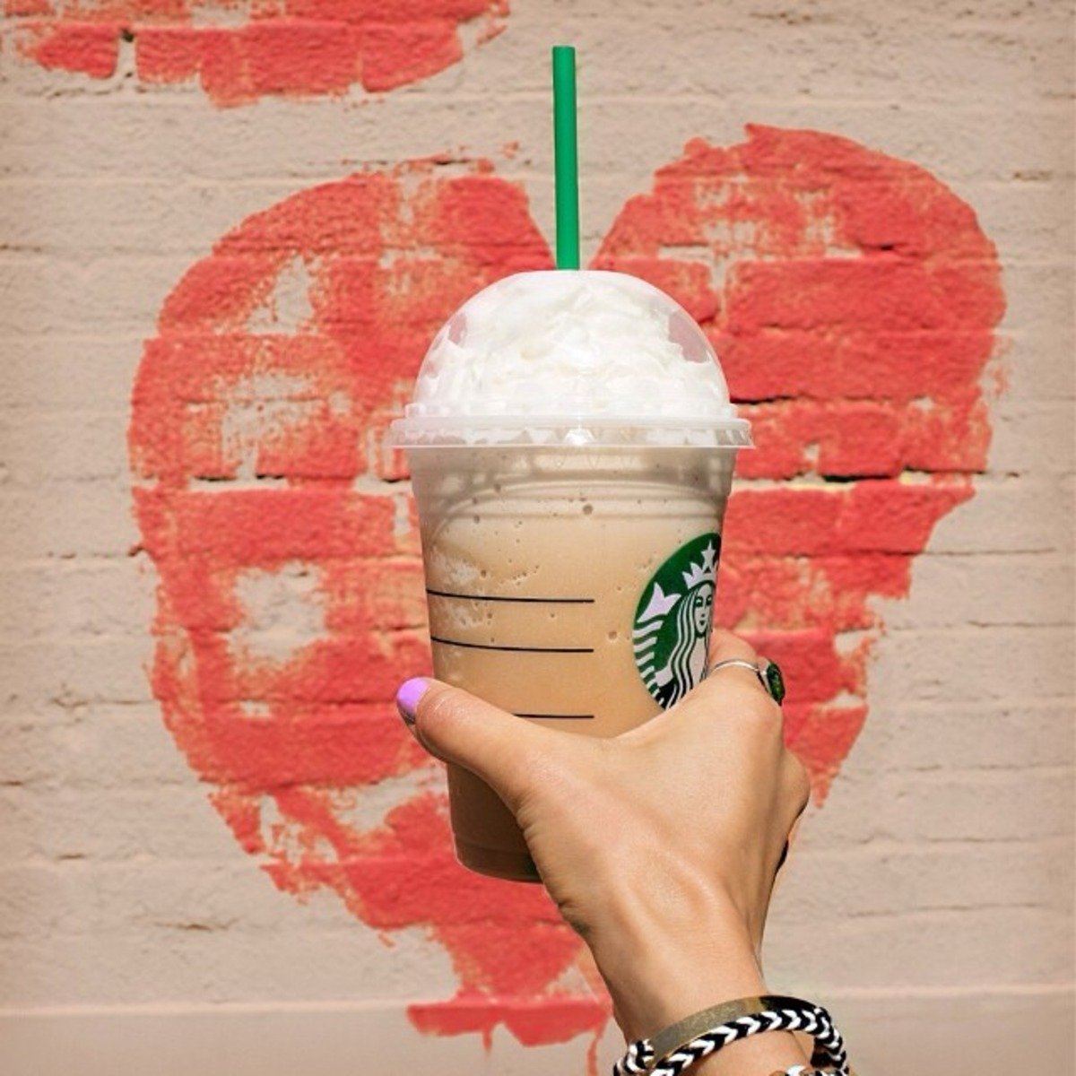 hand showing cup of starbucks hazelnut frappuccino with heart in background