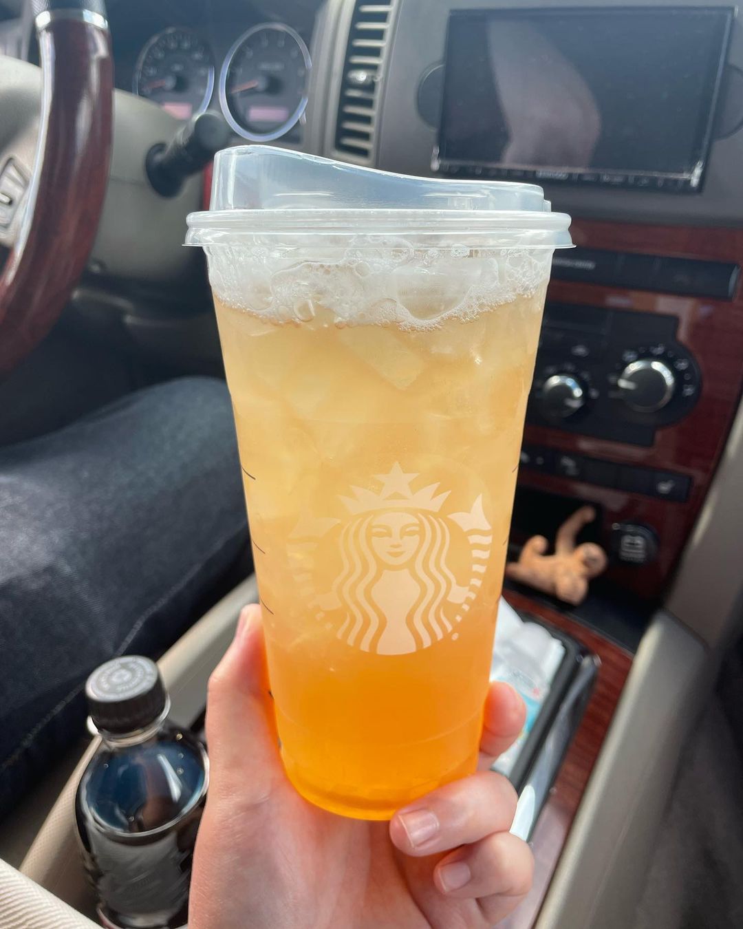 hand showing cup of starbucks iced peach green tea lemonade in car
