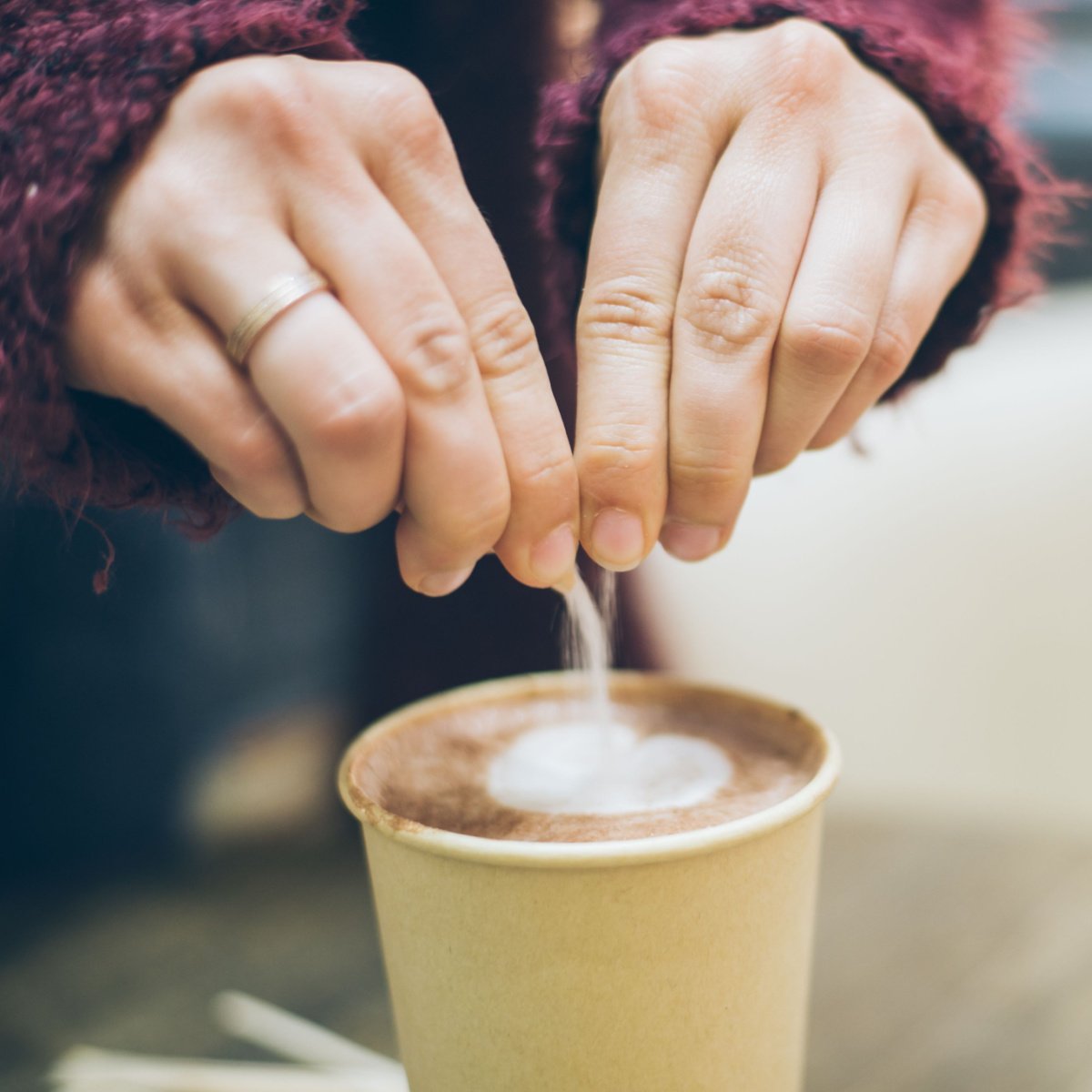 hands pouring sugar from sachet into cup of coffee