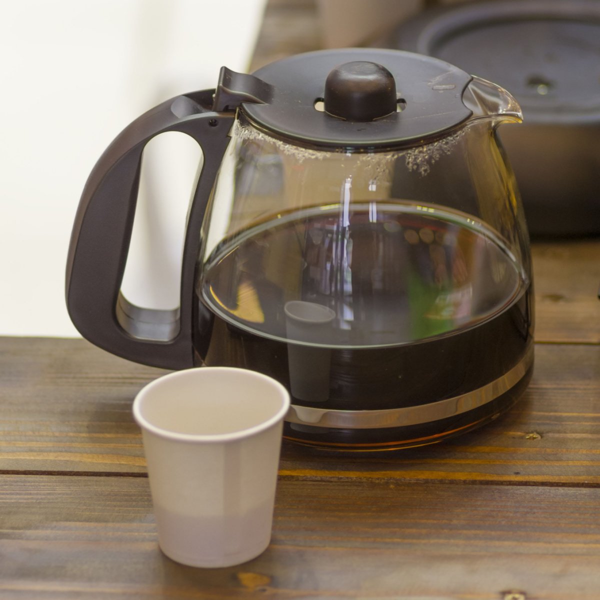 leftover coffee in clear glass carafe beside paper cup with unfinished coffee