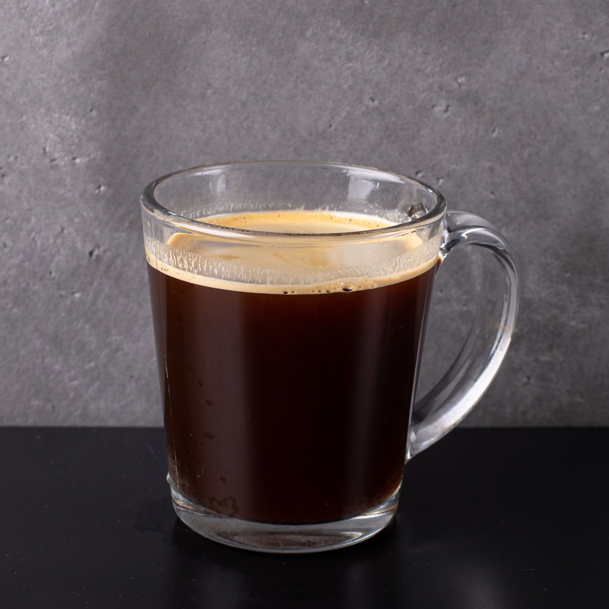 lungo in a glass mug on black table with cement background
