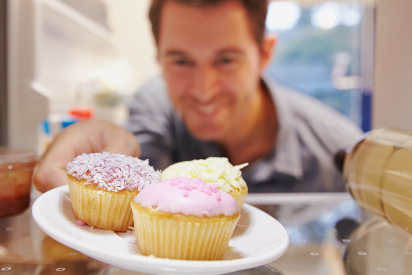 man places a plate of frosted cupcakes in the fridge
