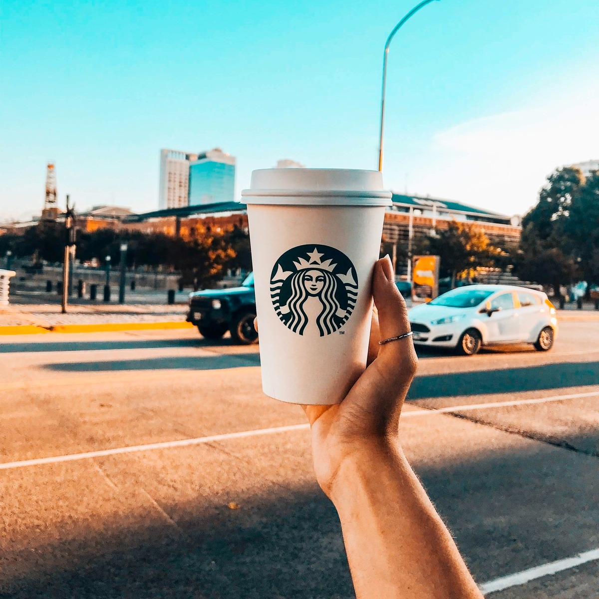 person holding up starbucs green and white disposable paper cup