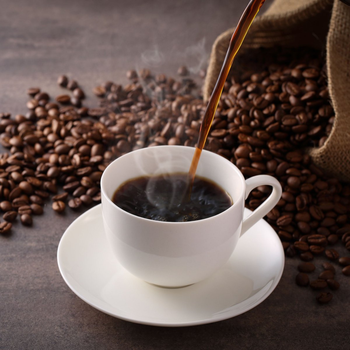 pouring coffee into white mug on saucer spilled coffee beans in background